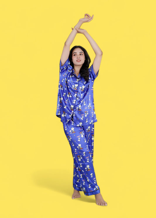 Woman wearing royal blue satin Snoopy print pyjama set with white piping, long pants, and short-sleeve shirt, nightwear by WakeUp Chicq.