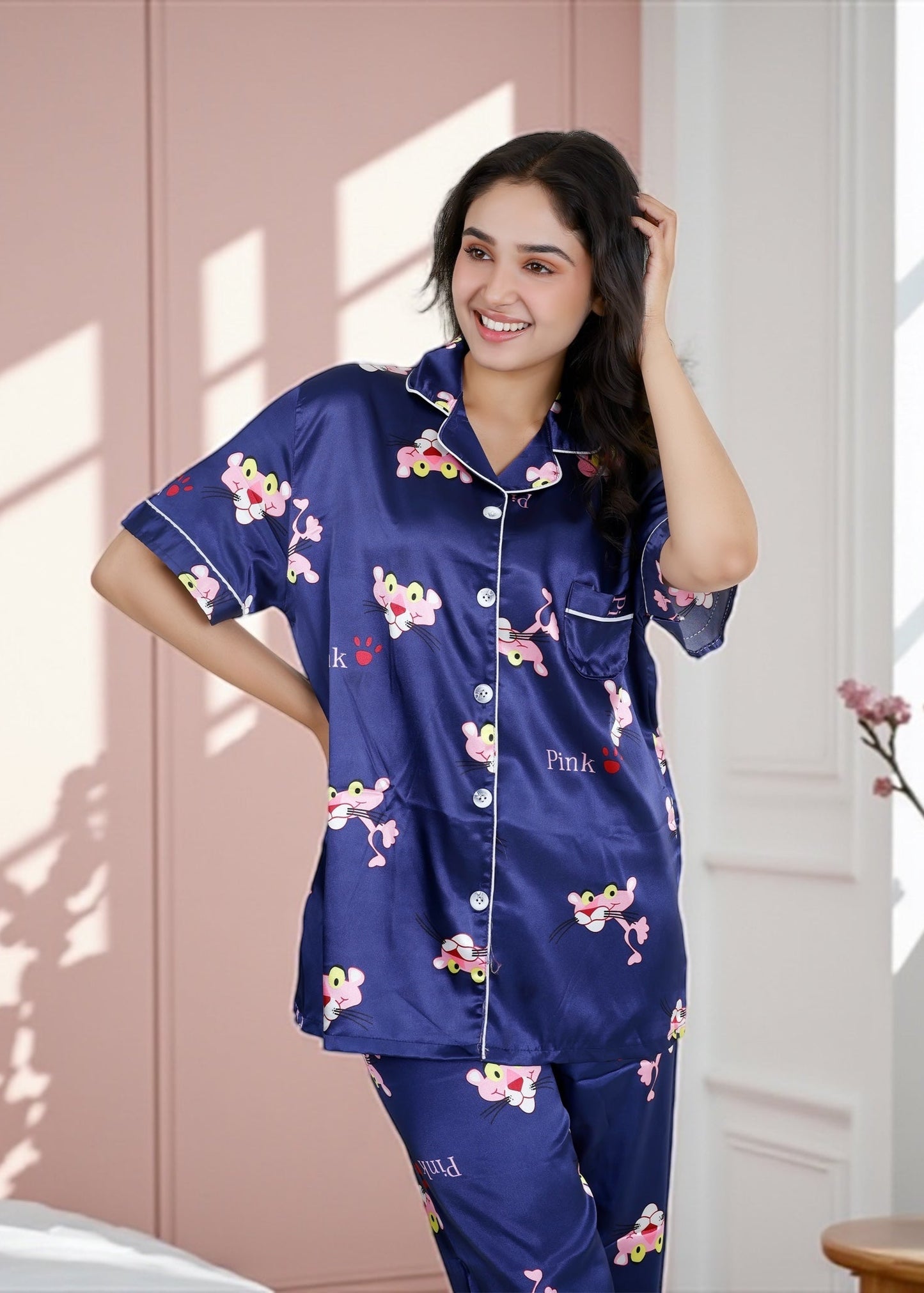 Woman wearing royal blue satin pyjama set with Pink Panther cartoon print, short-sleeve collared shirt and matching full-length pants, by WakeUp Chicq.