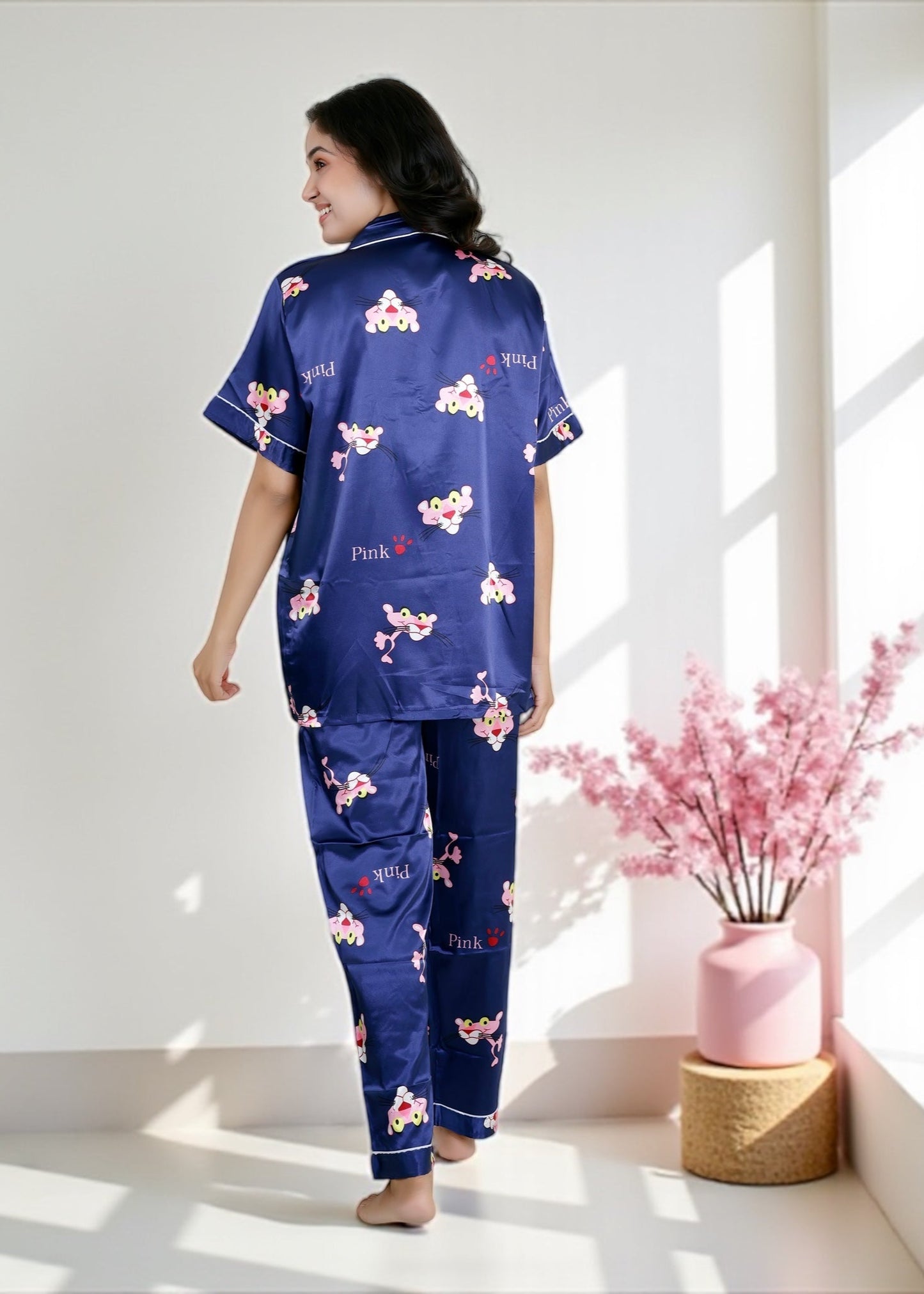 Woman wearing royal blue satin pyjama set with Pink Panther cartoon print, short-sleeve collared shirt and matching full-length pants, by WakeUp Chicq.
