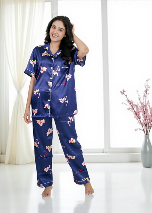Woman wearing royal blue satin pyjama set with Pink Panther cartoon print, short-sleeve collared shirt and matching full-length pants, by WakeUp Chicq.