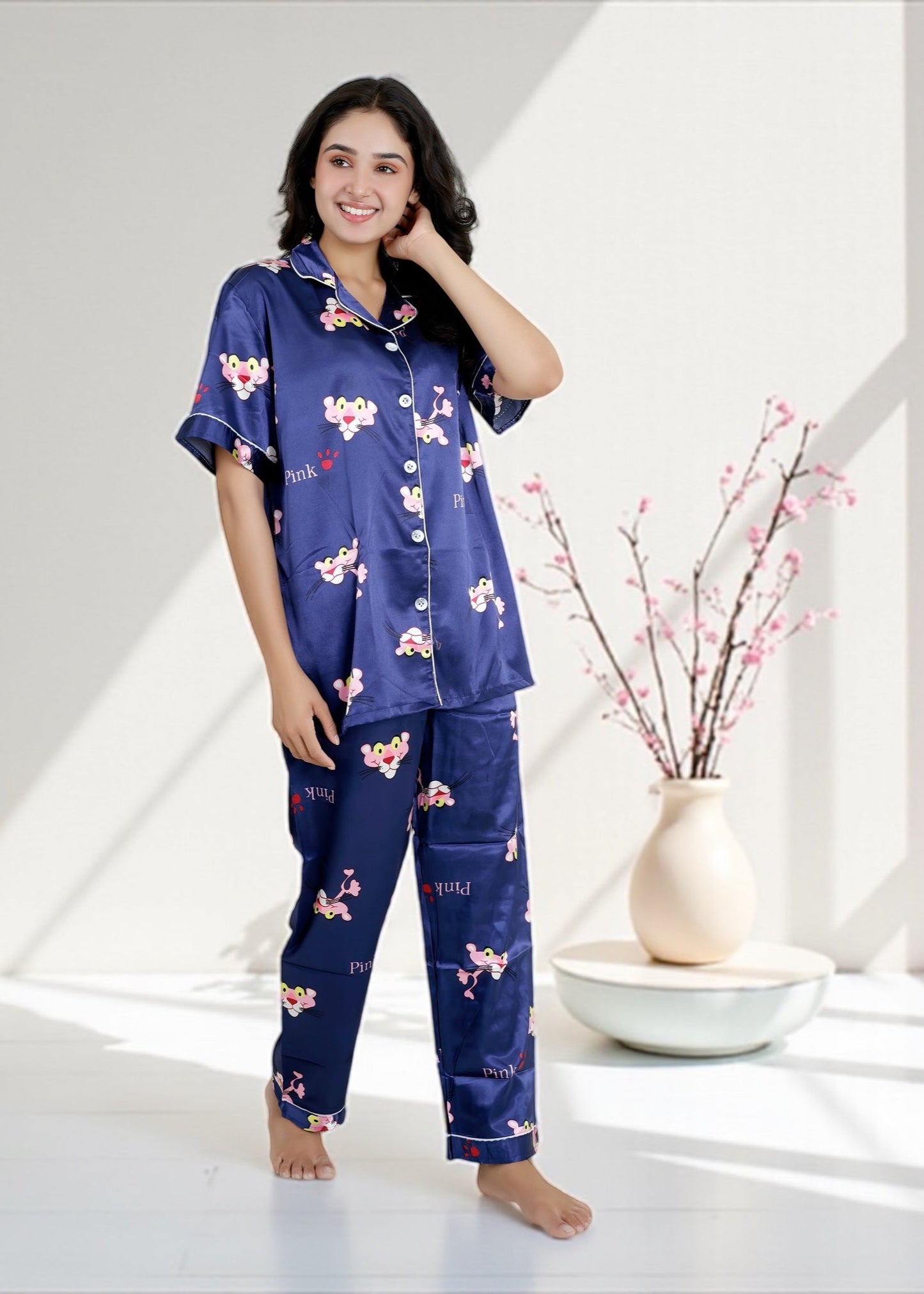 Woman wearing royal blue satin pyjama set with Pink Panther cartoon print, short-sleeve collared shirt and matching full-length pants, by WakeUp Chicq.