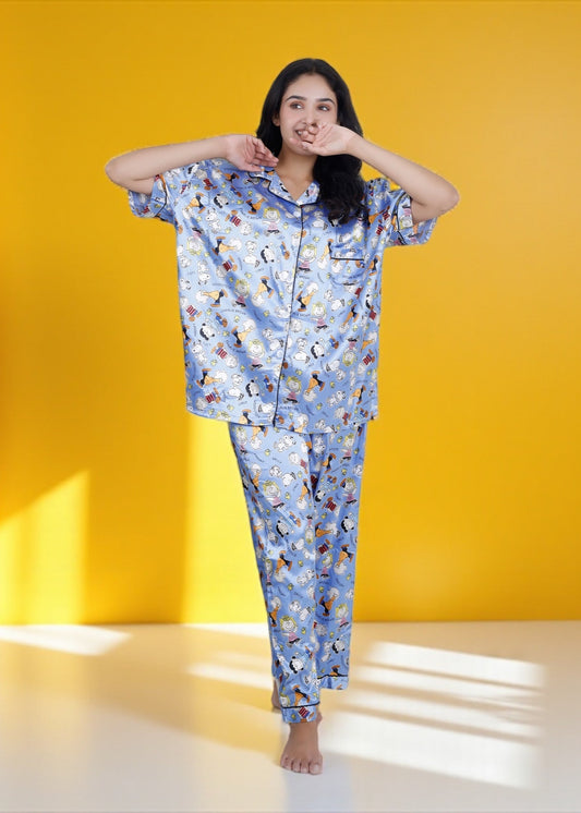Woman wearing sky blue satin pyjama set with Snoopy and Peanuts cartoon print, full-length luxury sleepwear by WakeUp Chicq.