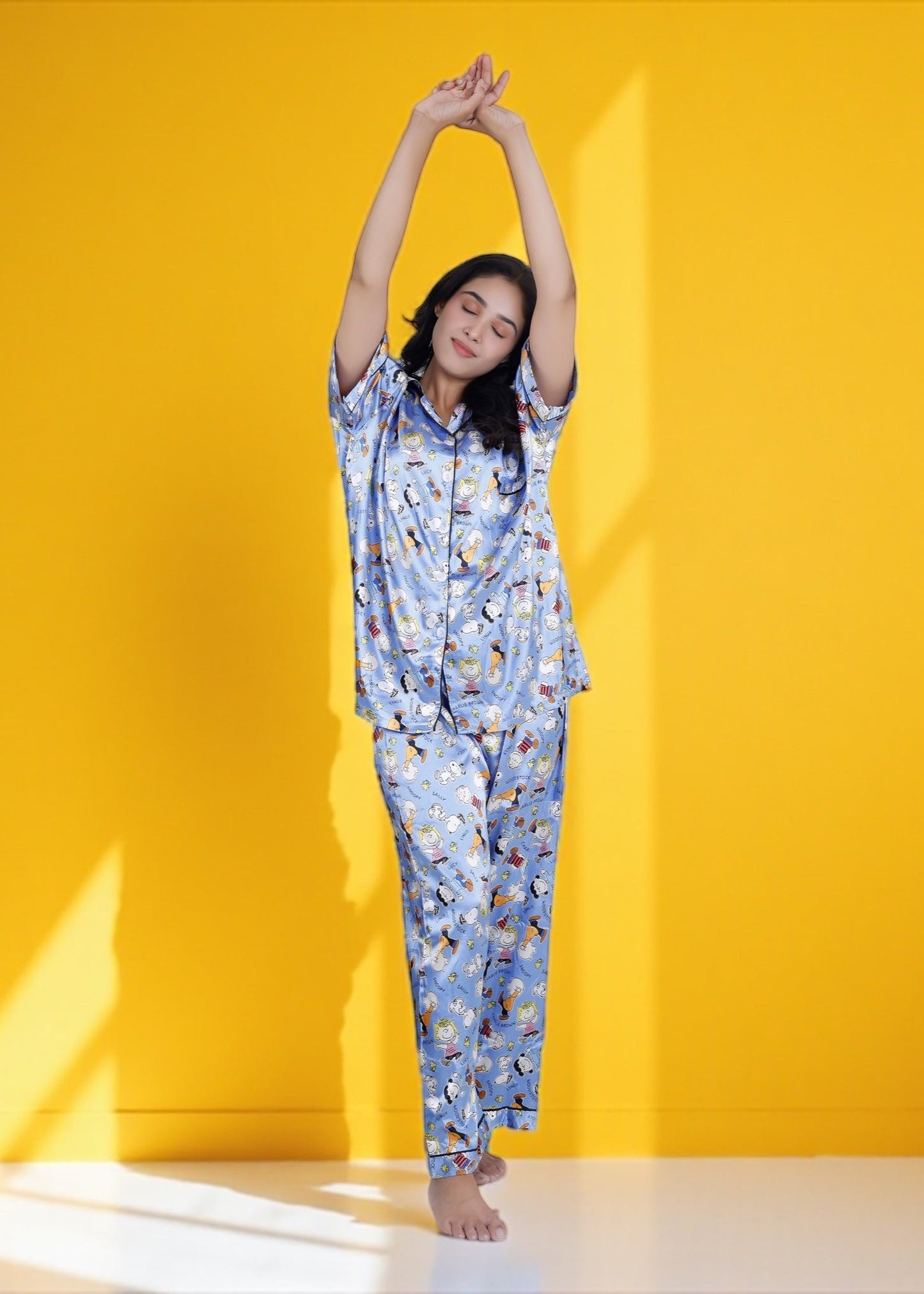 Woman wearing sky blue satin pyjama set with Snoopy and Peanuts cartoon print, full-length luxury sleepwear by WakeUp Chicq.