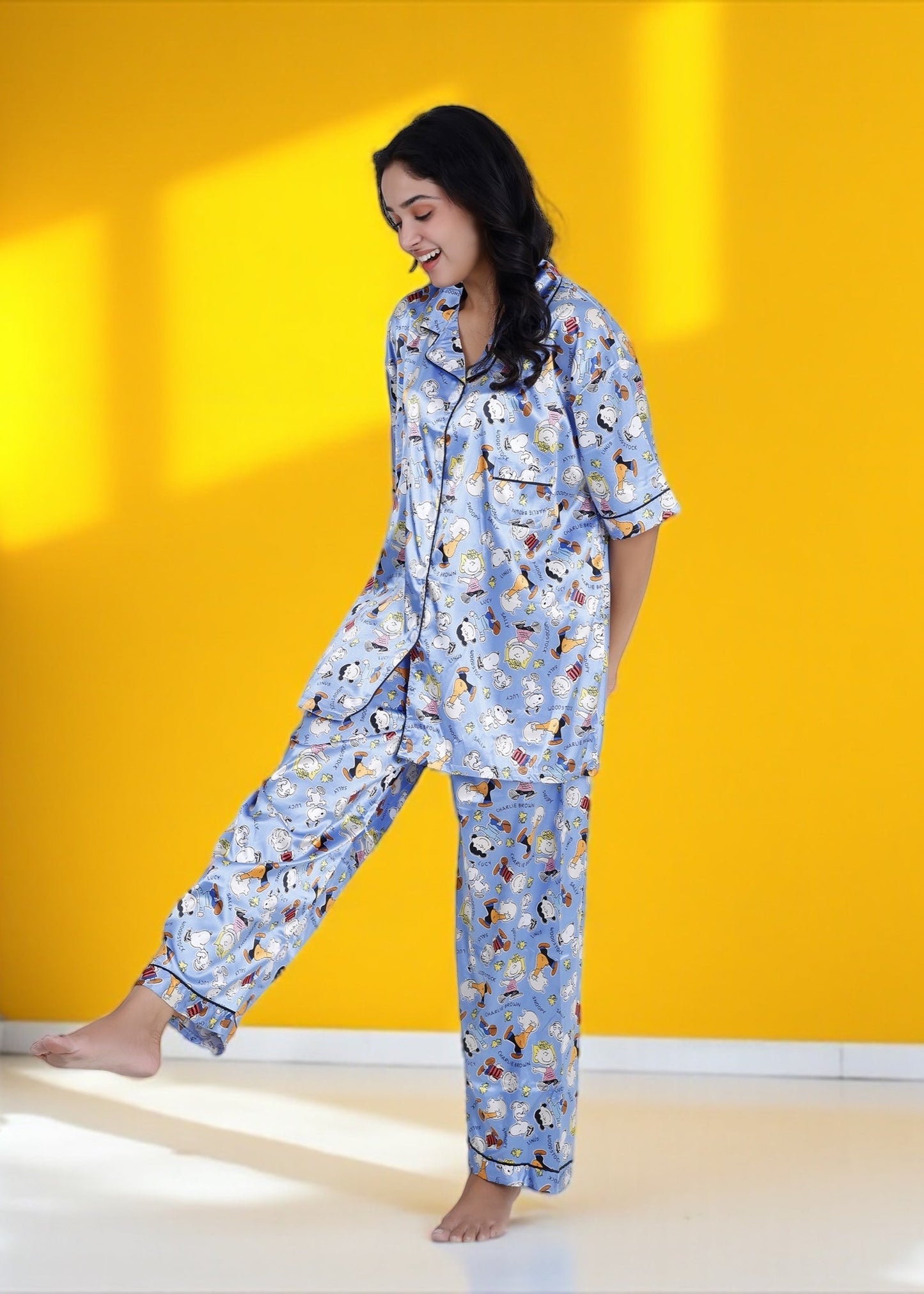 Woman wearing sky blue satin pyjama set with Snoopy and Peanuts cartoon print, full-length luxury sleepwear by WakeUp Chicq.