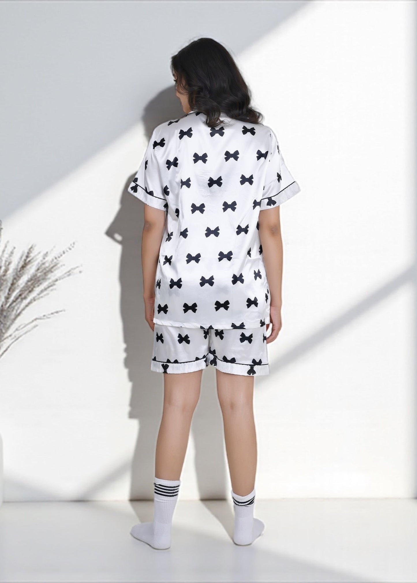 Woman wearing white satin shorts set with black bow print and black piping, elegant loungewear by WakeUp Chicq.
