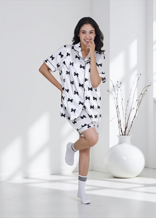 Woman wearing white satin shorts set with black bow print and black piping, elegant loungewear by WakeUp Chicq.