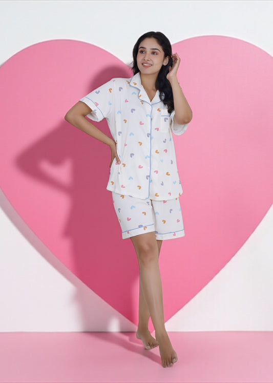 Woman wearing white cotton shorts set with multicolored heart print and blue piping. Breathable and cute sleepwear by WakeUp Chicq.