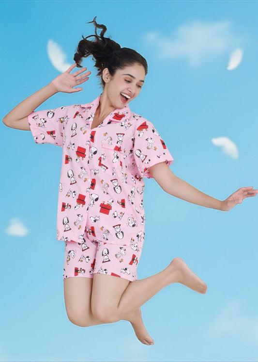Woman in pink cotton shorts set with Snoopy and red doghouse cartoon print, nightshirt-style loungewear by WakeUp Chicq.