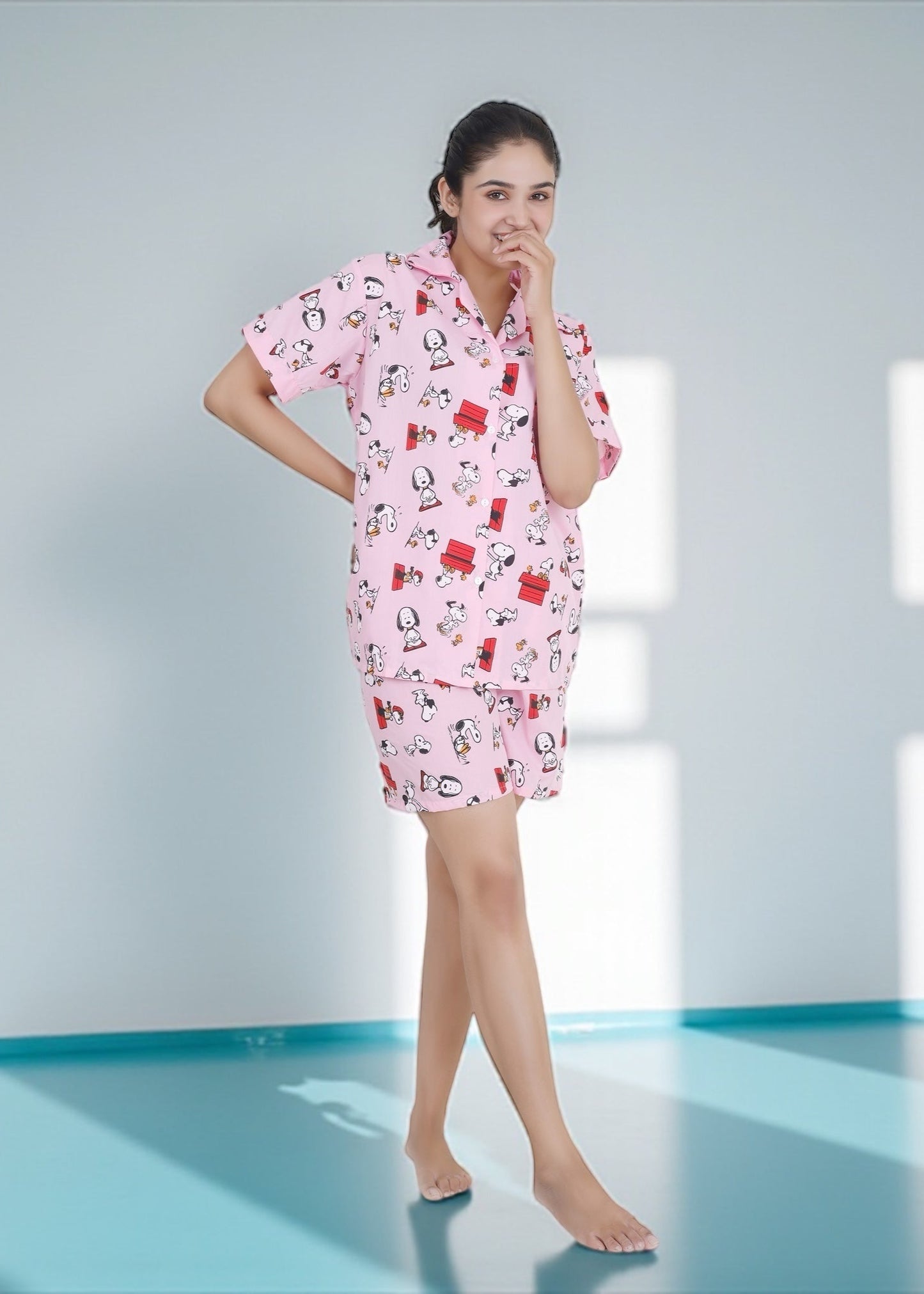 Woman in pink cotton shorts set with Snoopy and red doghouse cartoon print, nightshirt-style loungewear by WakeUp Chicq.