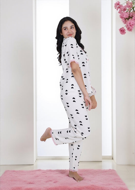 Woman wearing white crushed crepe pyjama set with black heart print and pink lace, by WakeUp Chicq.