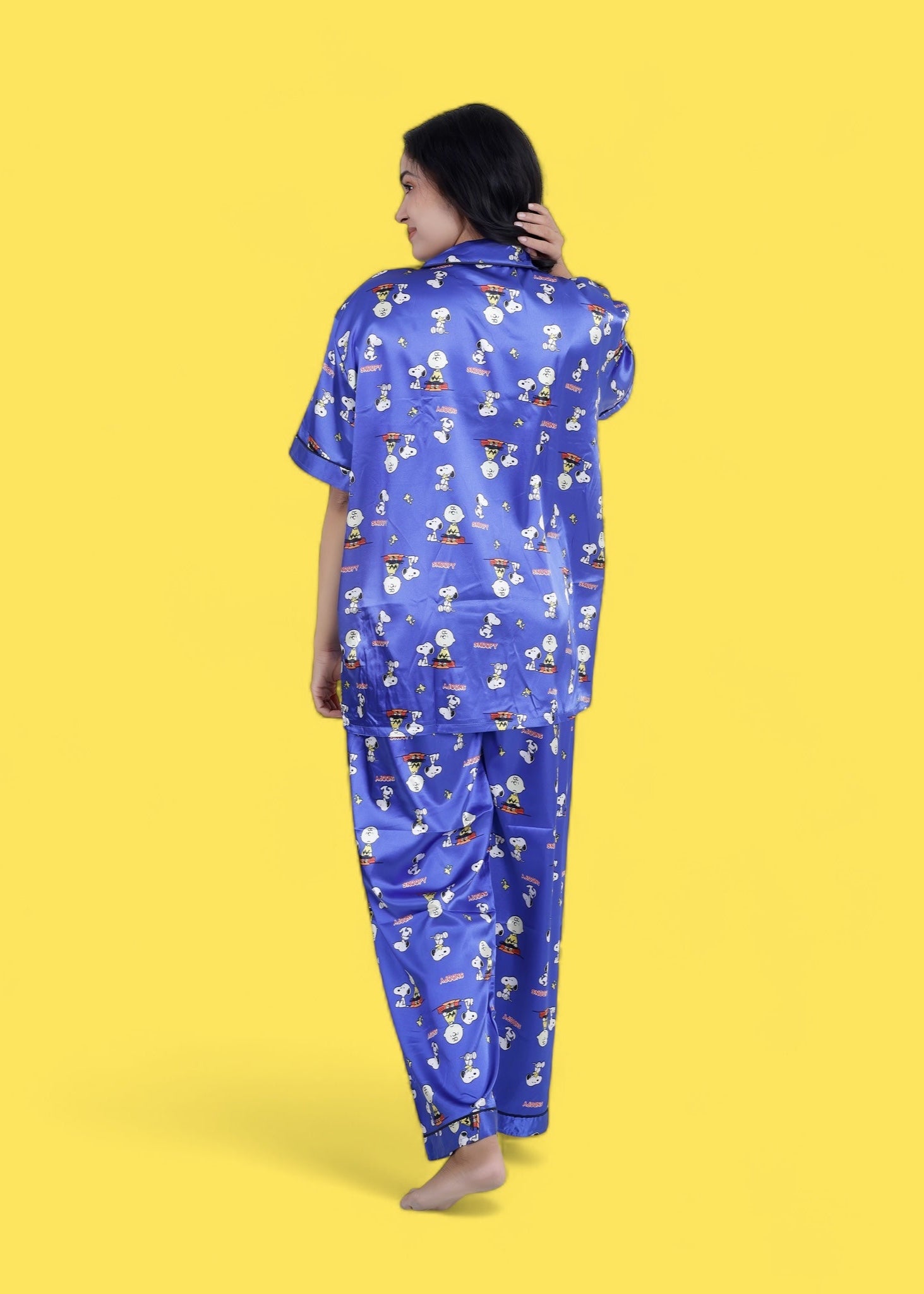 Woman wearing royal blue satin Snoopy print pyjama set with white piping, long pants, and short-sleeve shirt, nightwear by WakeUp Chicq.

