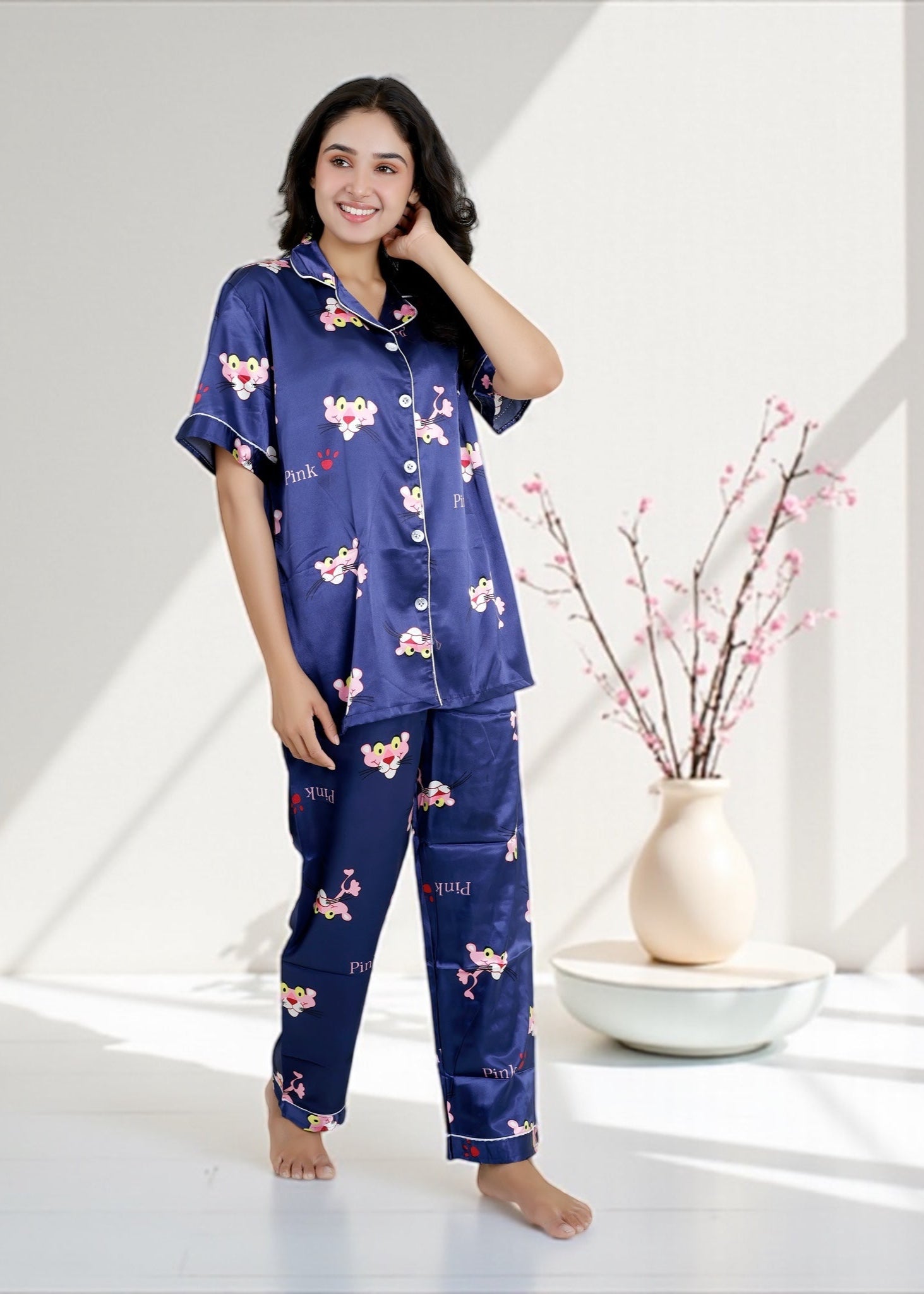 Woman wearing royal blue satin pyjama set with Pink Panther cartoon print, short-sleeve collared shirt and matching full-length pants, by WakeUp Chicq.

