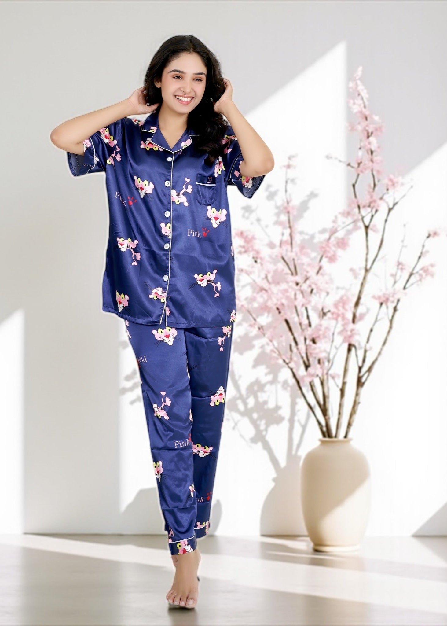 Woman wearing royal blue satin pyjama set with Pink Panther cartoon print, short-sleeve collared shirt and matching full-length pants, by WakeUp Chicq.

