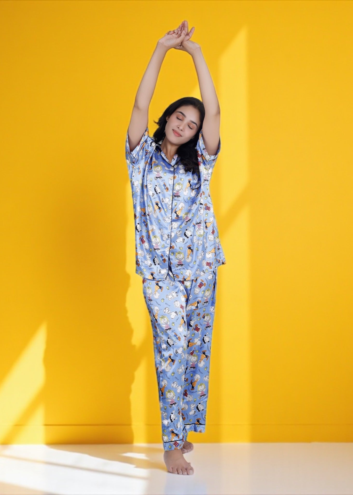 Woman wearing sky blue satin pyjama set with Snoopy and Peanuts cartoon print, full-length luxury sleepwear by WakeUp Chicq.