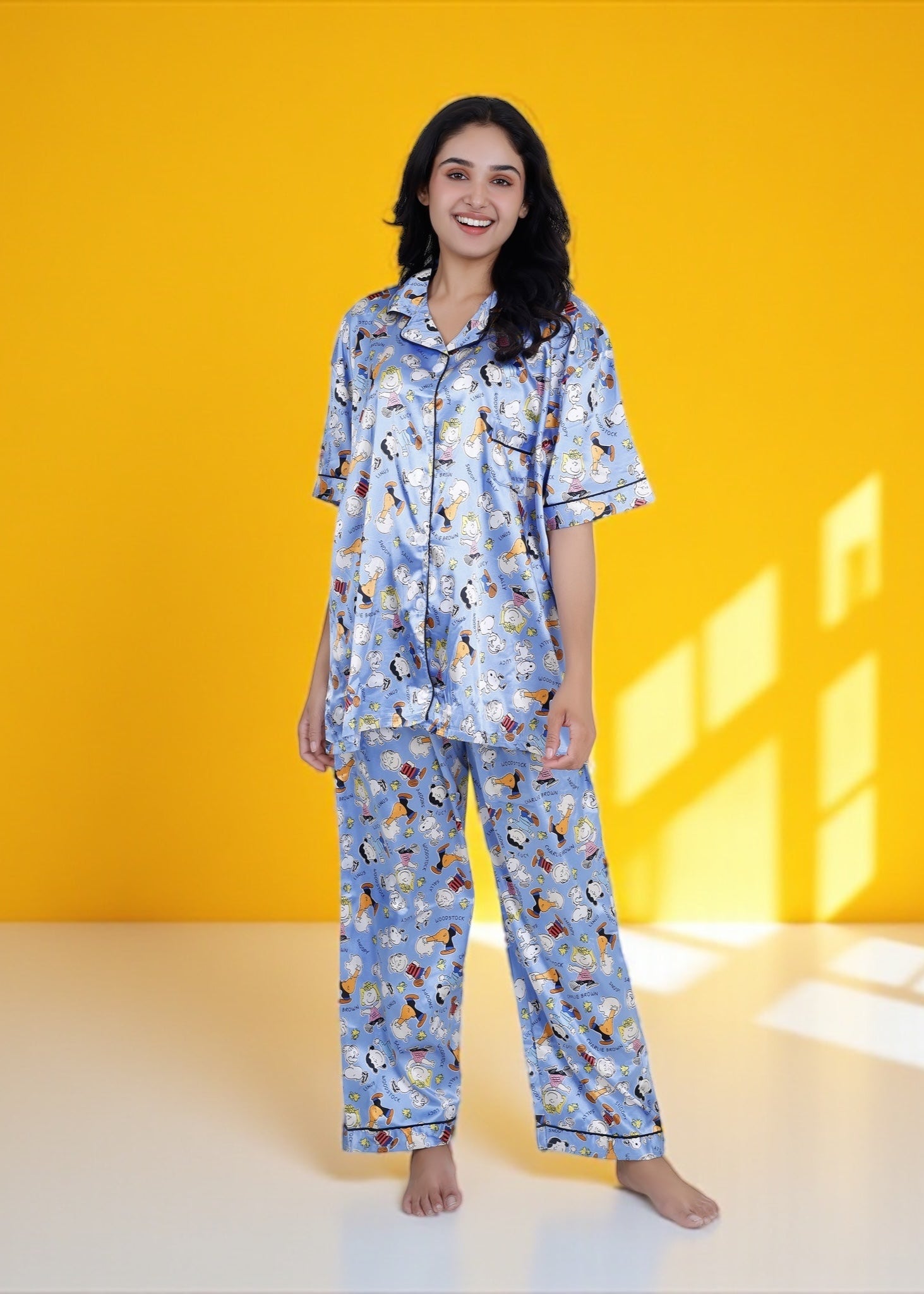 Woman wearing sky blue satin pyjama set with Snoopy and Peanuts cartoon print, full-length luxury sleepwear by WakeUp Chicq.