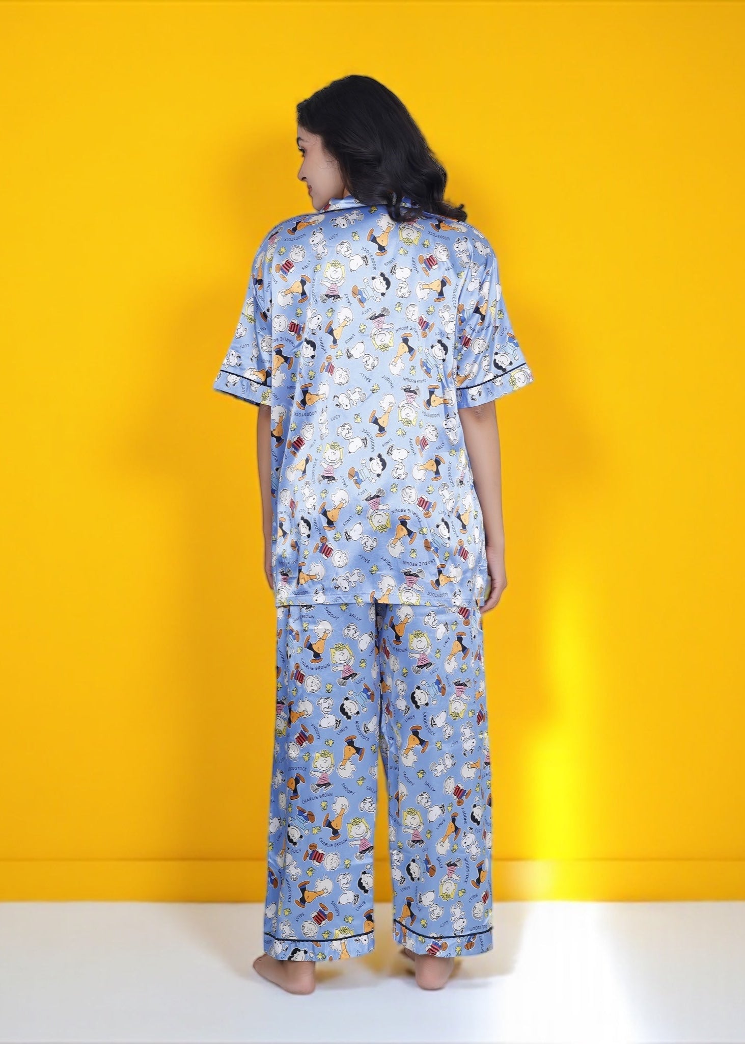 Woman wearing sky blue satin pyjama set with Snoopy and Peanuts cartoon print, full-length luxury sleepwear by WakeUp Chicq.