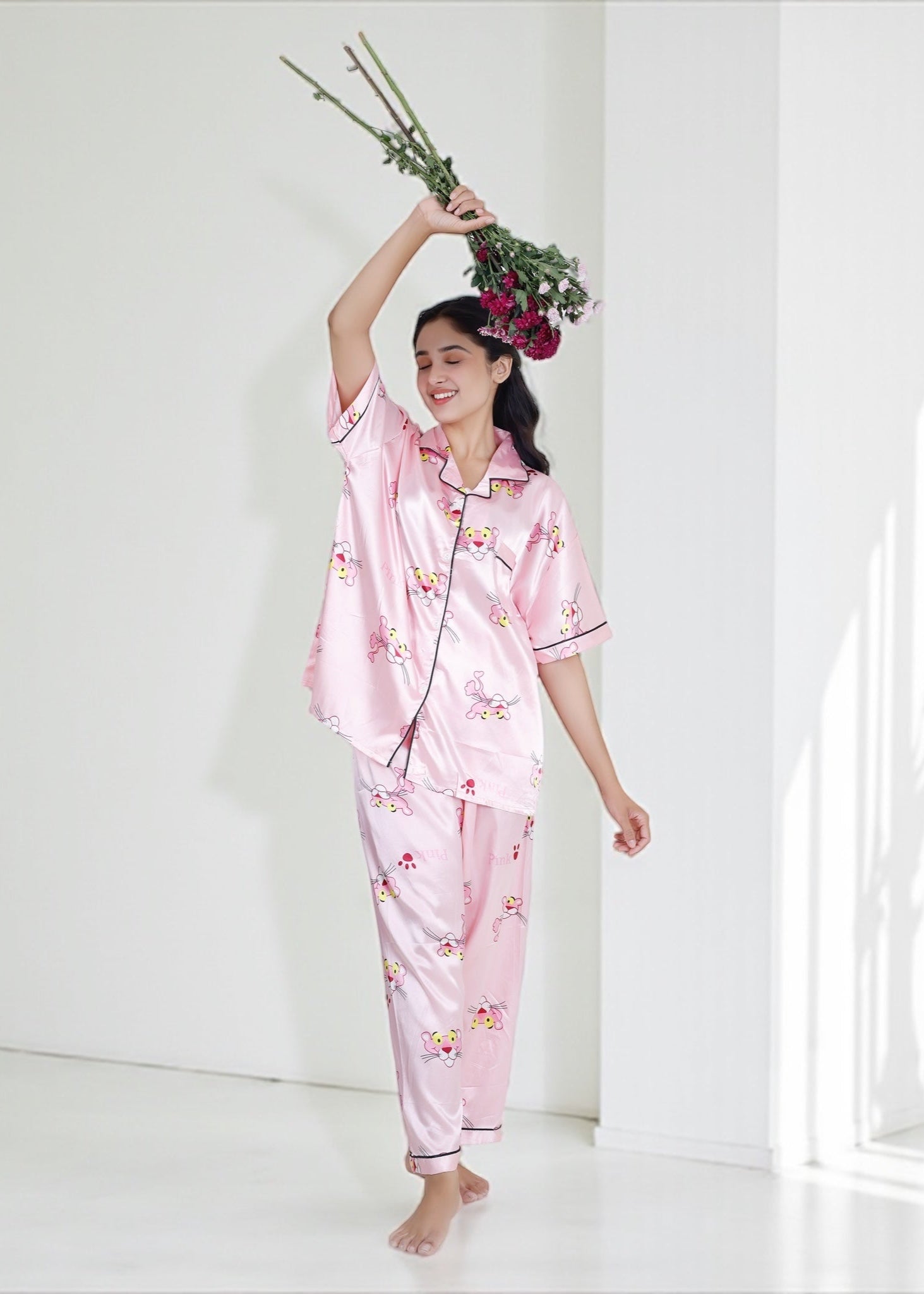 Woman wearing baby pink satin pyjama set with Pink Panther cartoon print and black piping, luxe loungewear by WakeUp Chicq.

