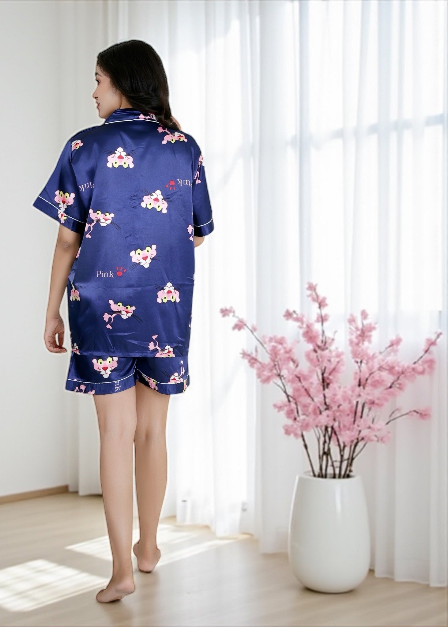 Woman wearing royal blue satin shorts set with vibrant Pink Panther cartoon print, short-sleeve collared shirt and matching shorts, by WakeUp Chicq.

