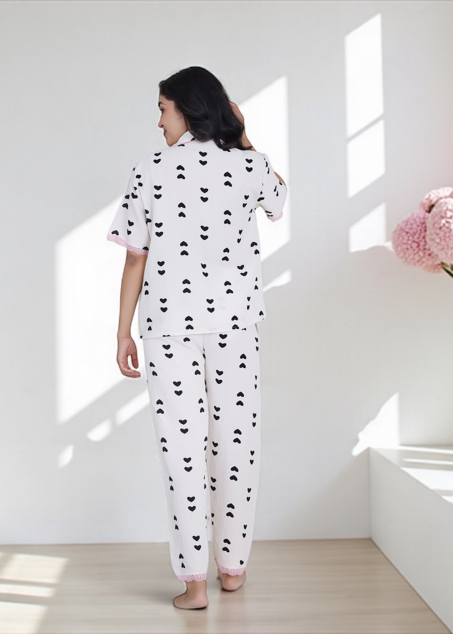 Woman wearing white crushed crepe pyjama set with black heart print and pink lace, by WakeUp Chicq.