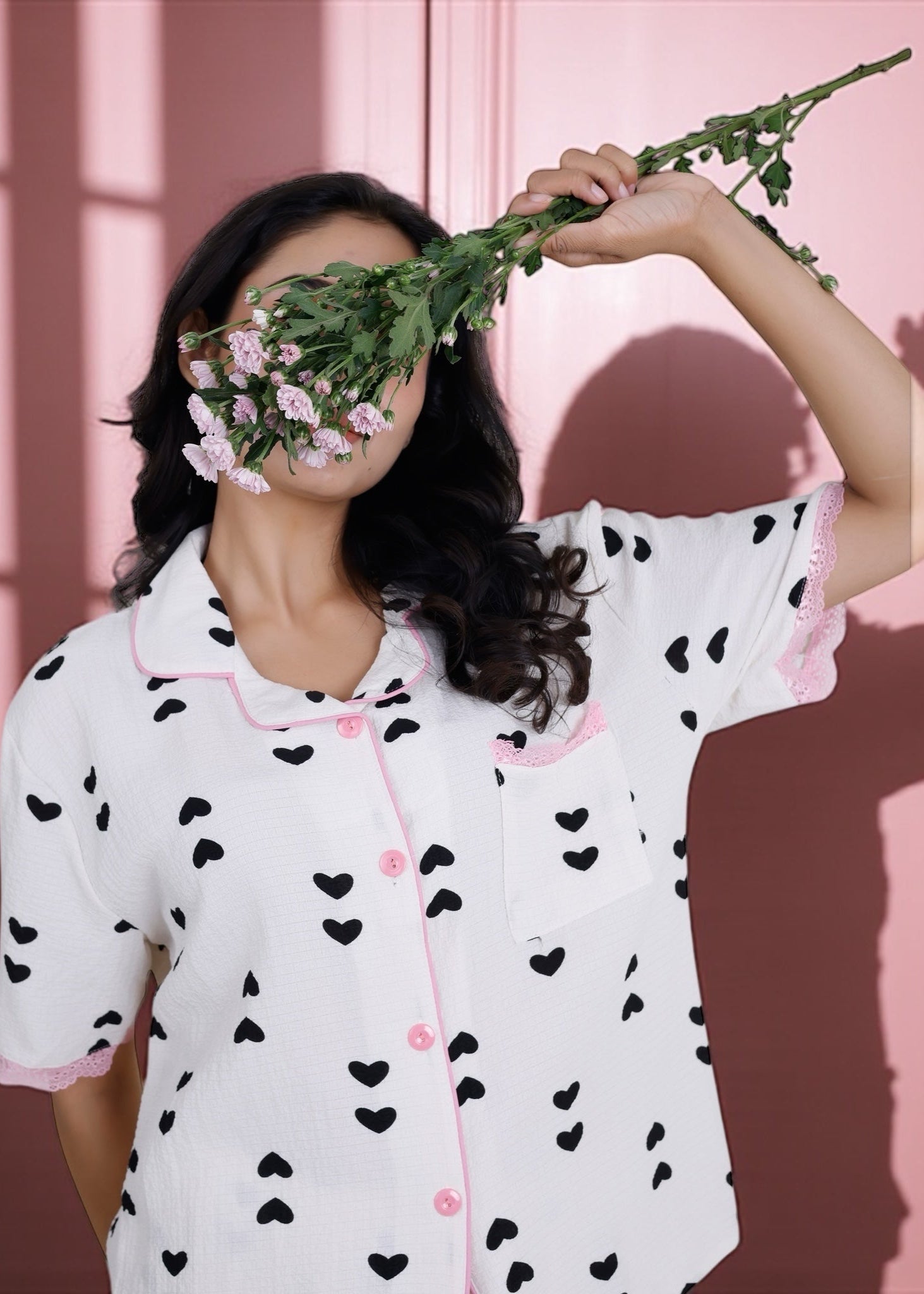 Woman wearing white crushed crepe pyjama set with black heart print and pink lace, by WakeUp Chicq.