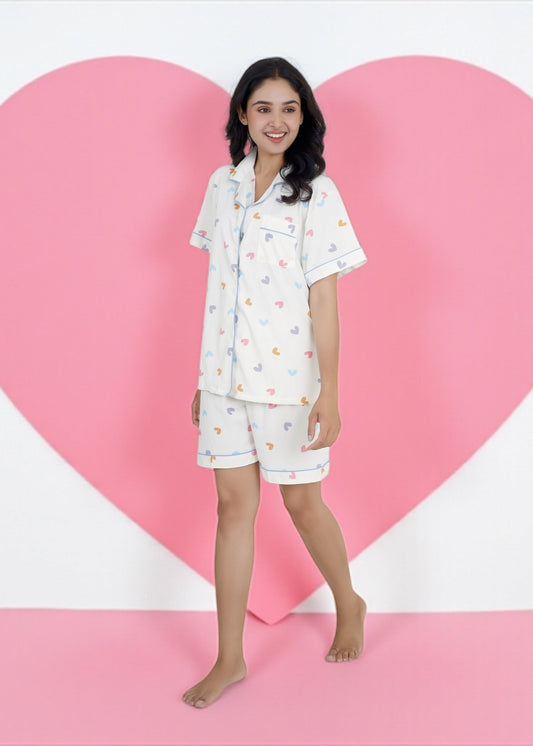 Woman wearing white cotton shorts set with multicolored heart print and blue piping. Breathable and cute sleepwear by WakeUp Chicq.

