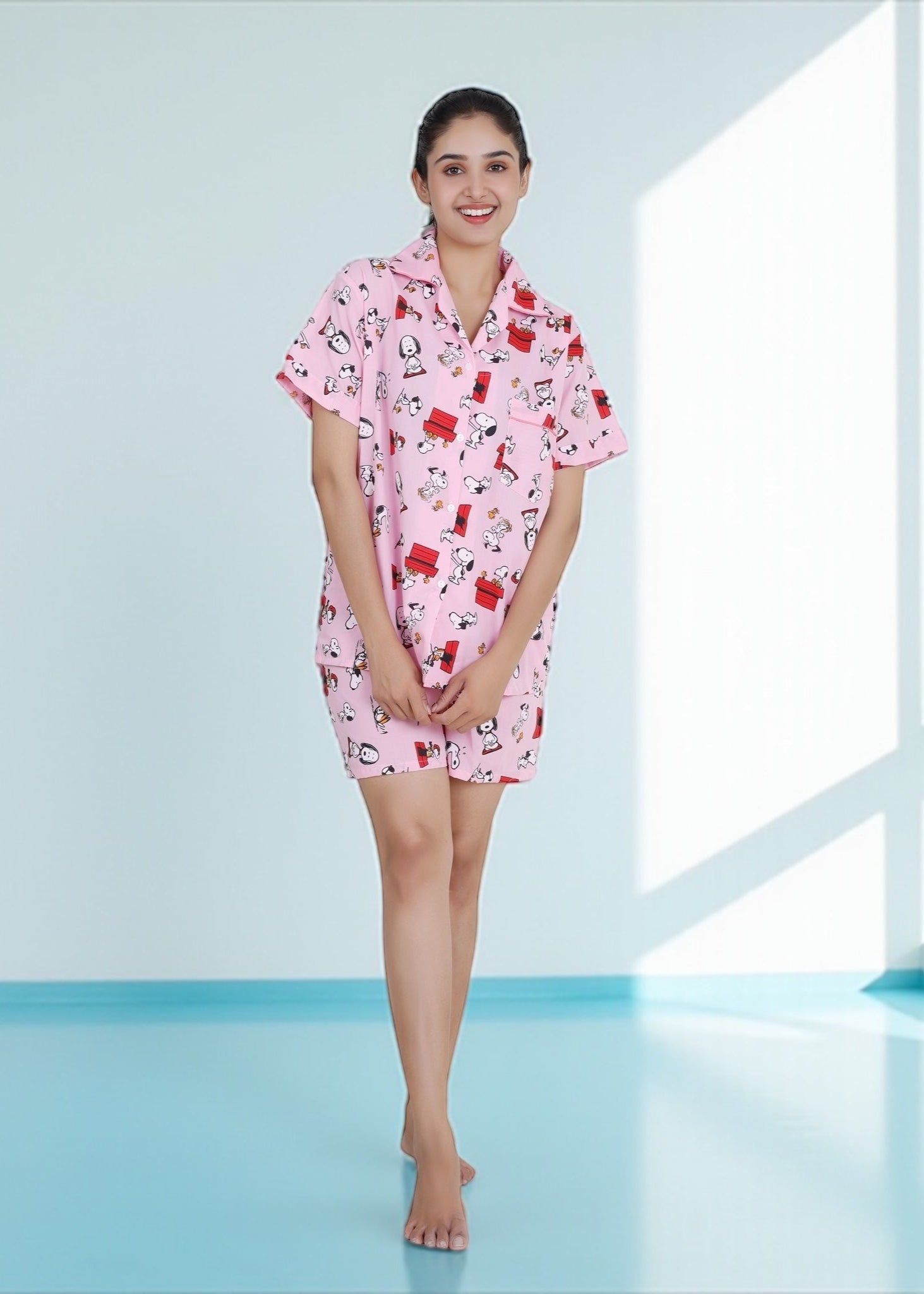 Woman in pink cotton shorts set with Snoopy and red doghouse cartoon print, nightshirt-style loungewear by WakeUp Chicq.

